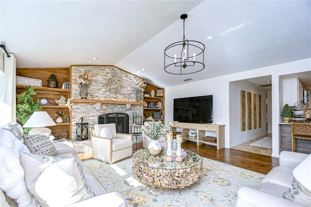 living room with lofted ceiling, a fireplace, light hardwood / wood-style floors, built in shelves, and a chandelier