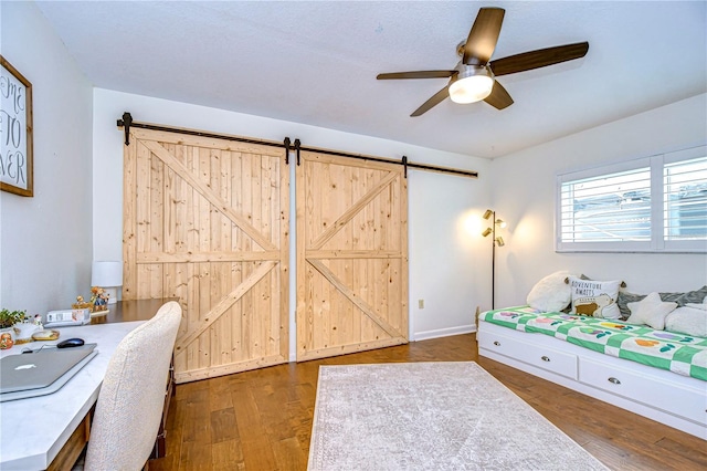 bedroom with a barn door, dark wood-type flooring, and ceiling fan