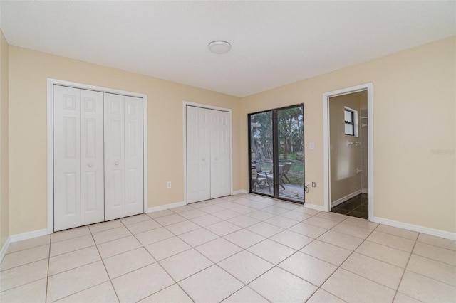 unfurnished bedroom with access to exterior, light tile patterned floors, and two closets