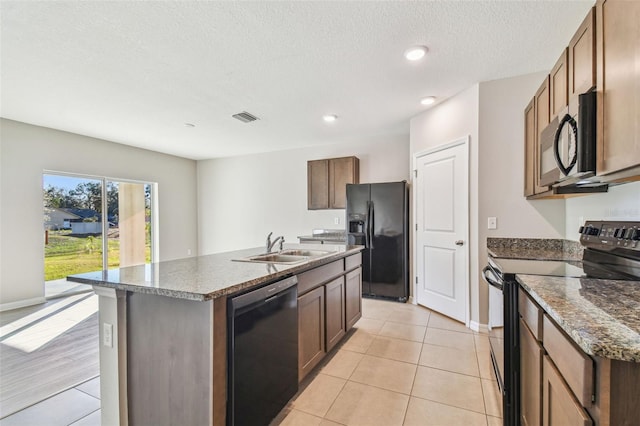 kitchen with sink, light tile patterned floors, a kitchen island with sink, black appliances, and a textured ceiling