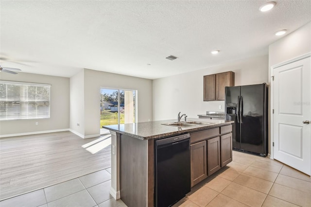 kitchen featuring sink, a kitchen island with sink, light tile patterned floors, black appliances, and dark brown cabinets