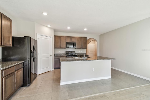 kitchen with dark stone countertops, sink, black appliances, and an island with sink