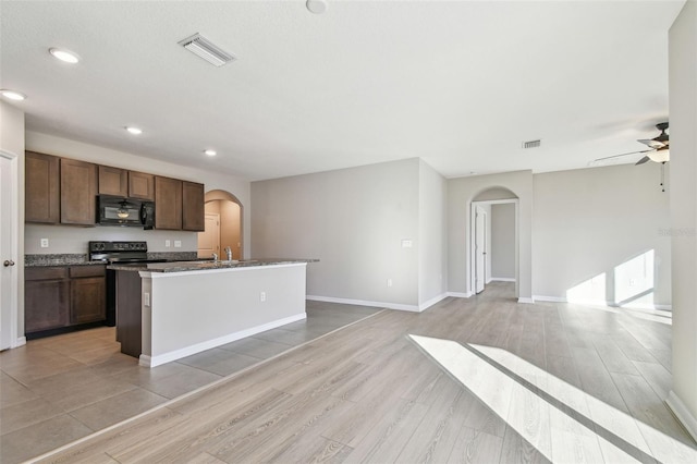 kitchen with sink, light wood-type flooring, an island with sink, ceiling fan, and black appliances