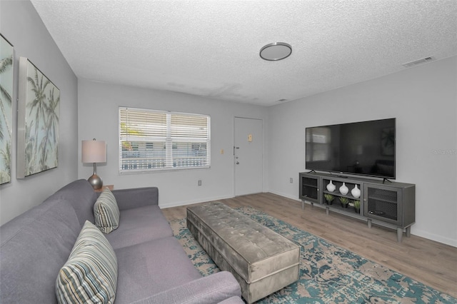 living room featuring baseboards, a textured ceiling, visible vents, and wood finished floors