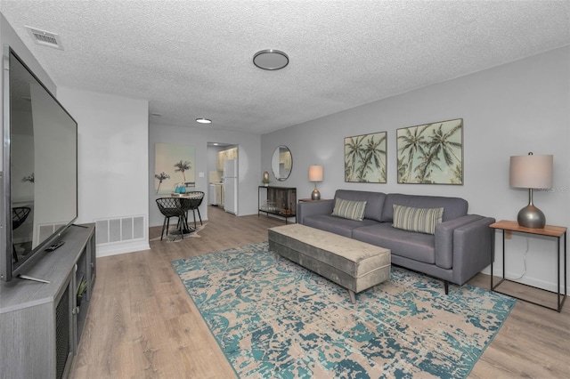 living room featuring visible vents, a textured ceiling, baseboards, and wood finished floors