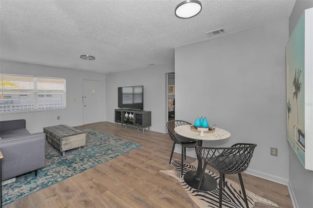 living room with visible vents, a textured ceiling, baseboards, and wood finished floors