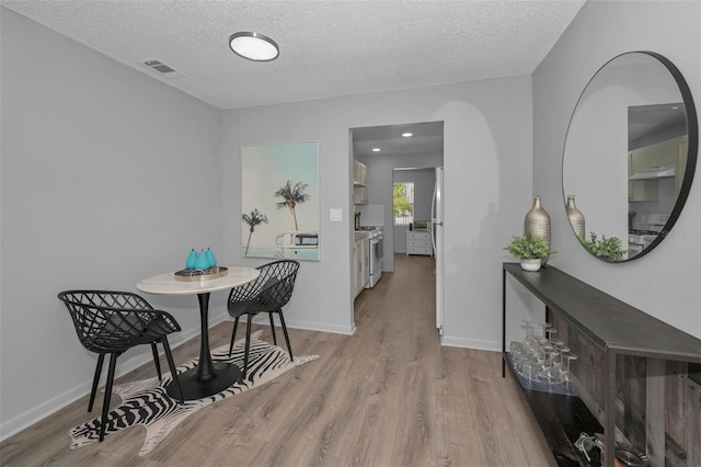 dining room featuring visible vents, a textured ceiling, baseboards, and wood finished floors