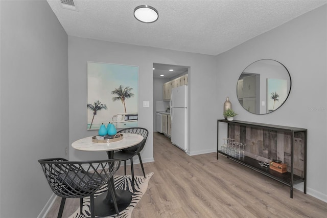 dining area with a textured ceiling, light wood finished floors, and baseboards