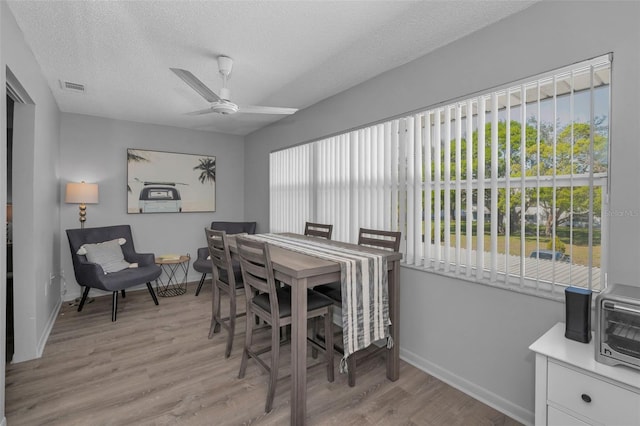 dining space with visible vents, ceiling fan, a textured ceiling, light wood-type flooring, and baseboards