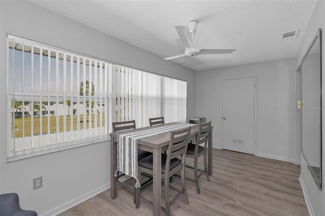 dining space featuring visible vents, ceiling fan, a textured ceiling, wood finished floors, and baseboards