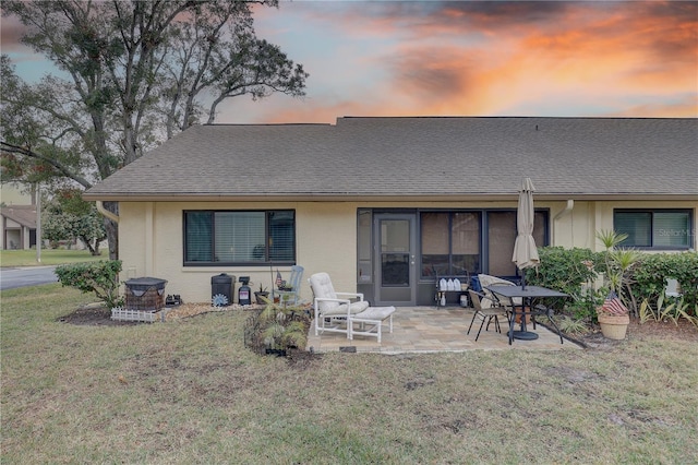 back house at dusk featuring a patio and a lawn