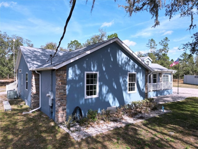 view of property exterior featuring stone siding, a lawn, and roof with shingles