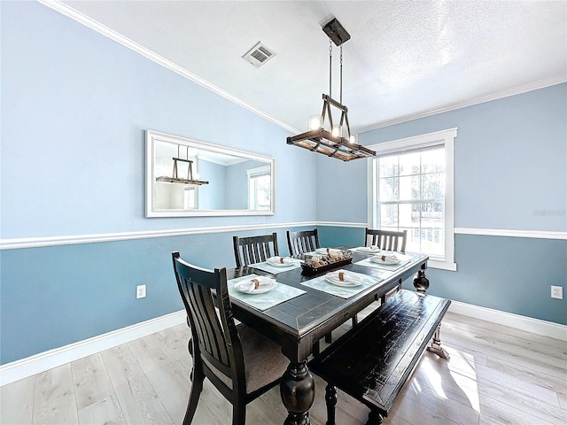 dining room featuring a textured ceiling, visible vents, baseboards, ornamental molding, and light wood-type flooring