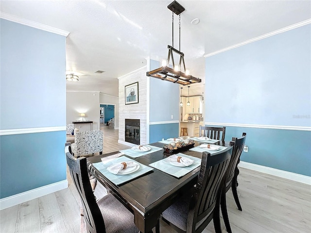 dining space featuring crown molding, visible vents, light wood-style floors, a tile fireplace, and baseboards