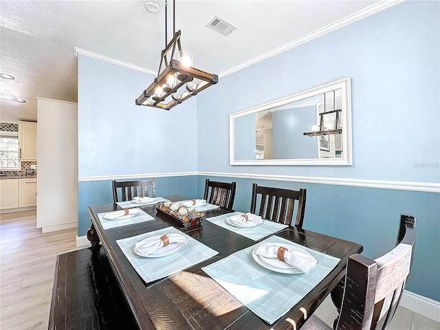 dining area with ornamental molding, light wood-type flooring, visible vents, and baseboards