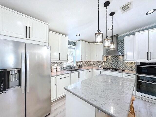 kitchen with wall chimney exhaust hood, white cabinetry, appliances with stainless steel finishes, and light stone counters