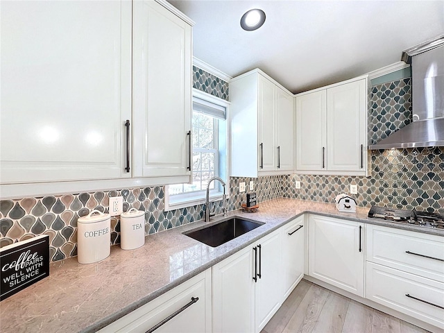 kitchen featuring stainless steel gas cooktop, wall chimney exhaust hood, sink, and white cabinets