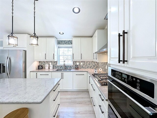 kitchen featuring a sink, white cabinets, hanging light fixtures, wall chimney range hood, and appliances with stainless steel finishes