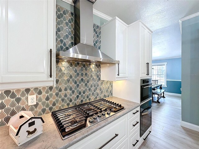 kitchen featuring white cabinetry, wall chimney exhaust hood, tasteful backsplash, oven, and stainless steel gas stovetop