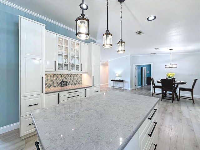 kitchen featuring light stone countertops, white cabinets, backsplash, and decorative light fixtures