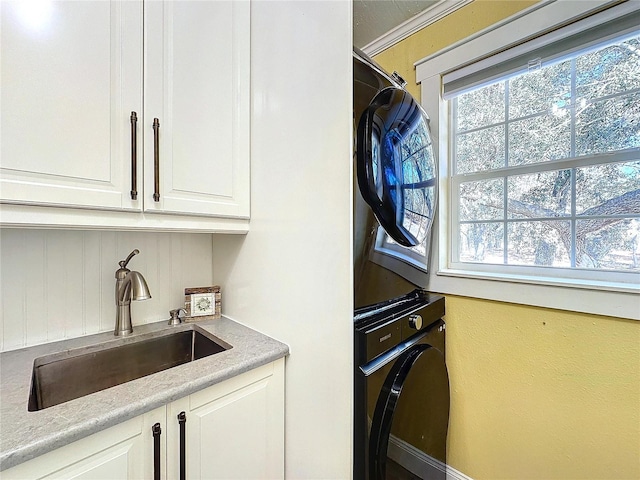 clothes washing area featuring cabinets, stacked washing maching and dryer, and sink