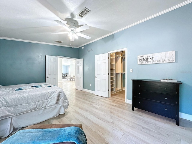 bedroom with light wood finished floors, visible vents, a spacious closet, ornamental molding, and baseboards