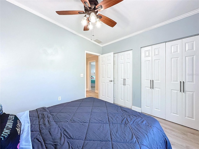 bedroom featuring ornamental molding, two closets, ceiling fan, and light hardwood / wood-style floors