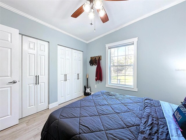 bedroom featuring vaulted ceiling, two closets, ornamental molding, ceiling fan, and light hardwood / wood-style floors