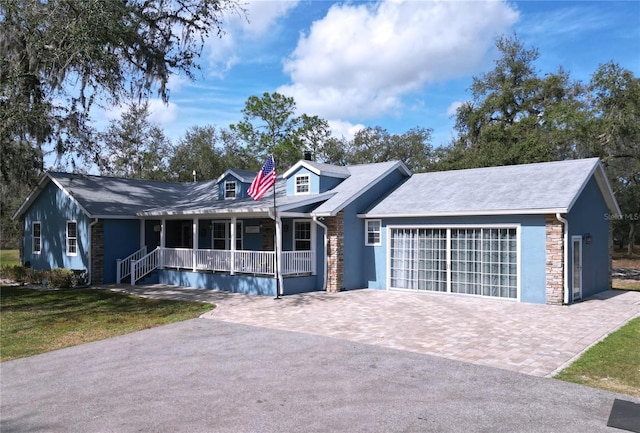 cape cod home with stone siding, an attached garage, covered porch, decorative driveway, and a front lawn