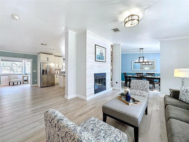 living room with ornamental molding, a large fireplace, built in features, and light wood-type flooring