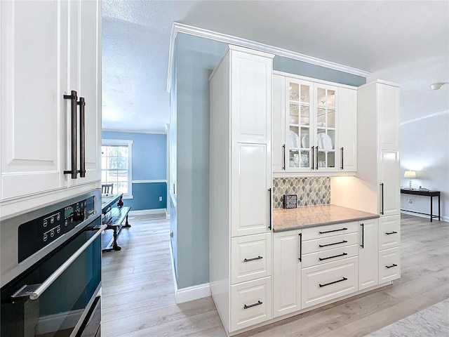 bar with backsplash, white cabinets, ornamental molding, wall oven, and light hardwood / wood-style flooring