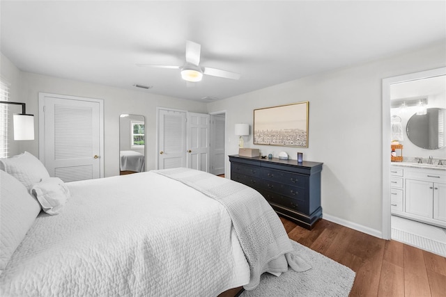 bedroom with sink, ceiling fan, dark hardwood / wood-style floors, connected bathroom, and multiple closets