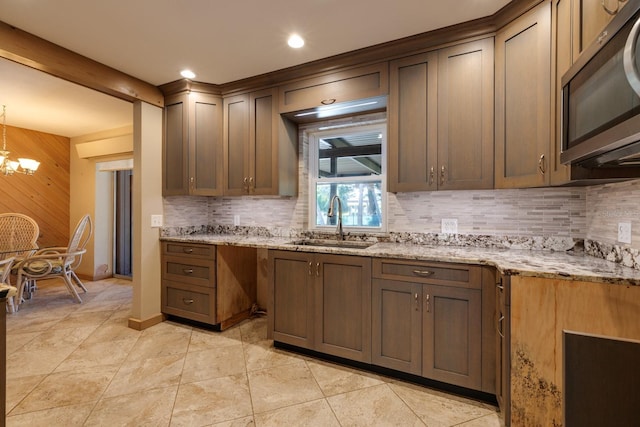 kitchen with sink, an inviting chandelier, hanging light fixtures, tasteful backsplash, and light stone countertops