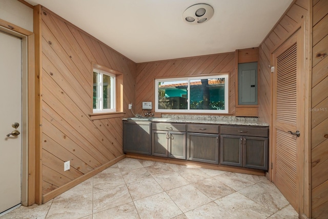 kitchen featuring light tile patterned floors, dark brown cabinets, electric panel, and wood walls