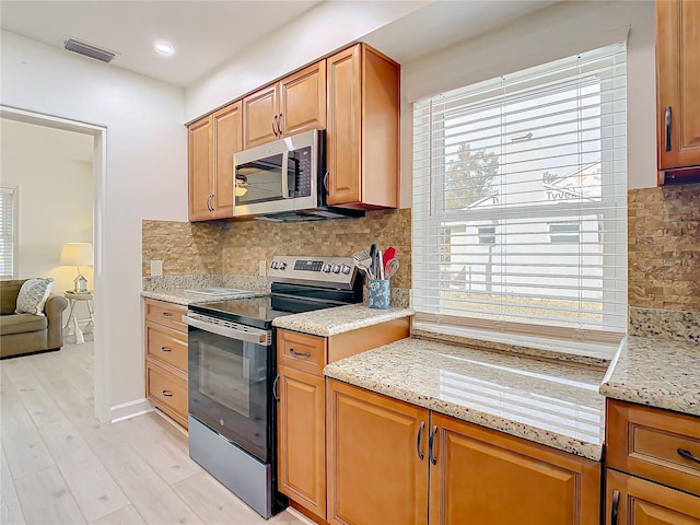 kitchen featuring stainless steel appliances, tasteful backsplash, light stone countertops, and light hardwood / wood-style flooring