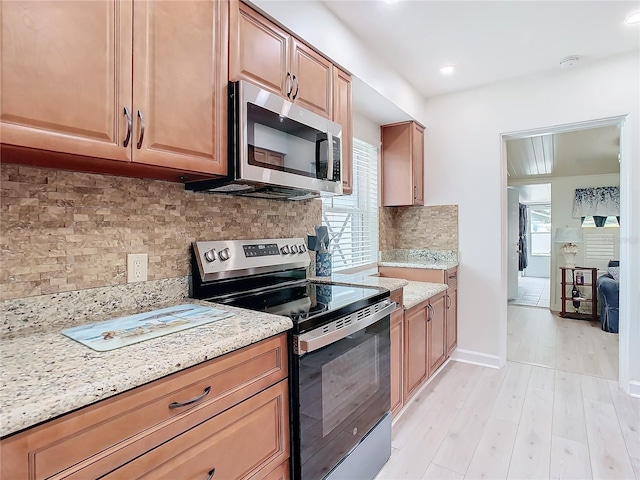 kitchen featuring appliances with stainless steel finishes, light stone countertops, light hardwood / wood-style floors, and decorative backsplash