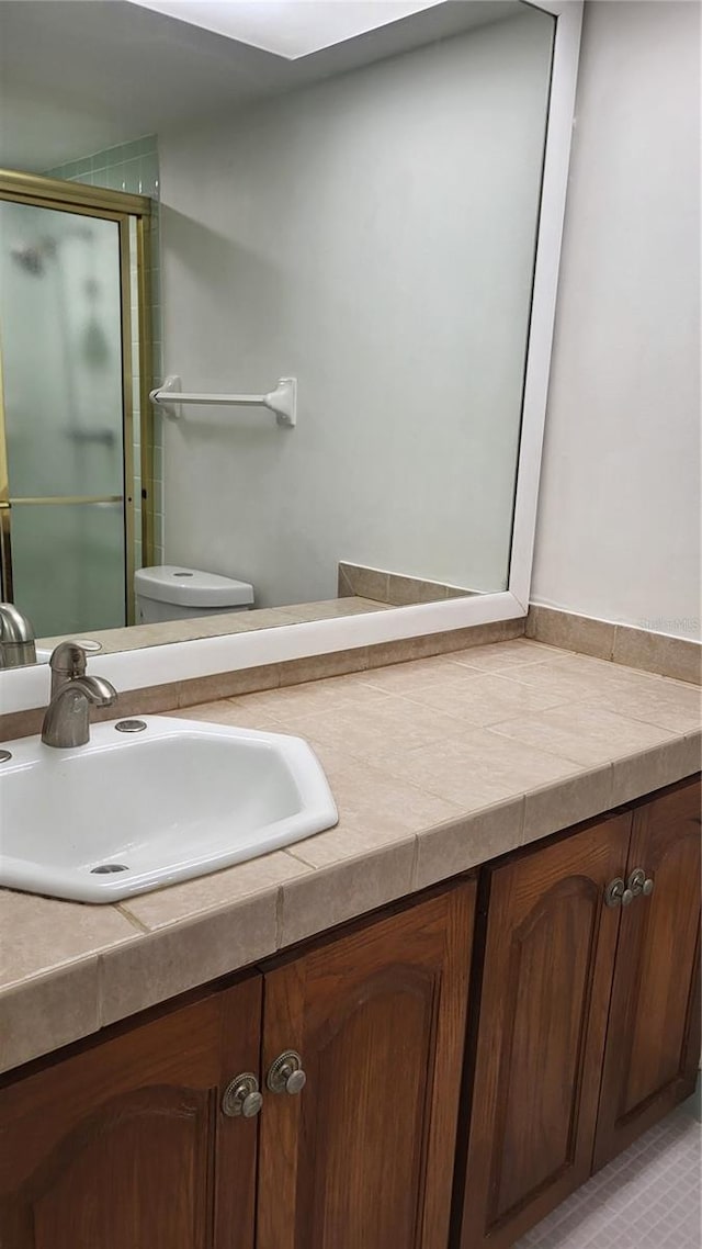 bathroom with vanity, toilet, a shower with shower door, and tile patterned flooring