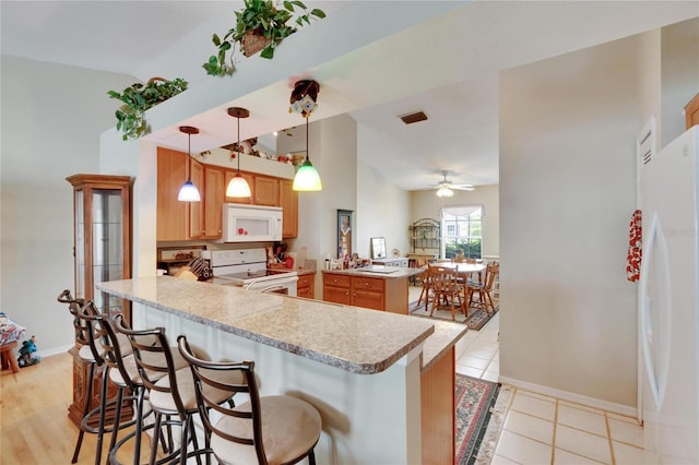 kitchen with a breakfast bar, ceiling fan, kitchen peninsula, pendant lighting, and white appliances