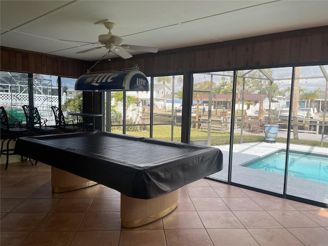 recreation room with tile patterned flooring, wooden walls, and ceiling fan