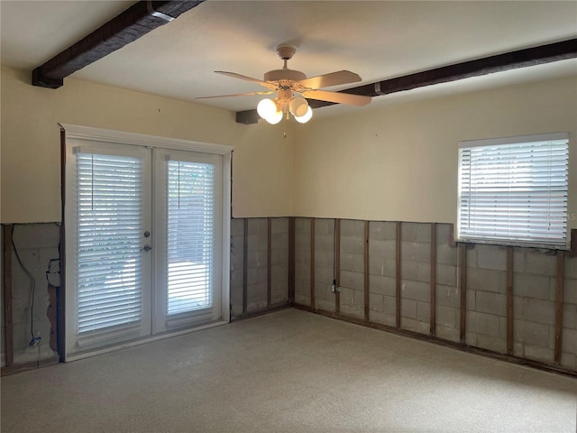 empty room with ceiling fan, plenty of natural light, french doors, and beamed ceiling