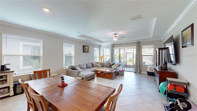 tiled dining room with ornamental molding, plenty of natural light, a tray ceiling, and a textured ceiling