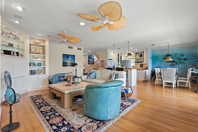 living room with ornamental molding, light hardwood / wood-style floors, ceiling fan, and built in shelves