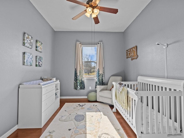 bedroom with wood-type flooring, a nursery area, and ceiling fan