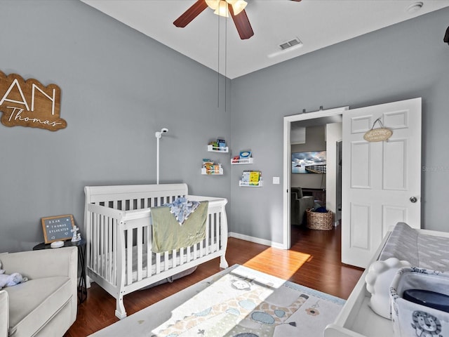 bedroom with a nursery area, ceiling fan, and dark hardwood / wood-style floors