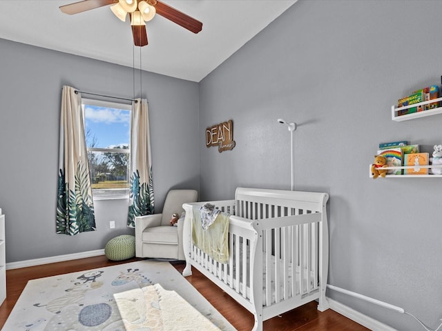 bedroom with dark wood-type flooring, ceiling fan, and a crib