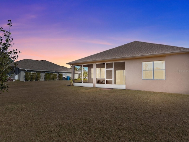 back house at dusk with a sunroom and a yard