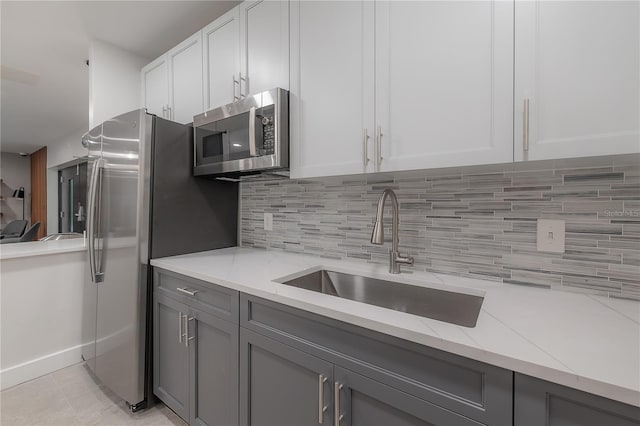 kitchen featuring sink, white cabinetry, backsplash, stainless steel appliances, and light stone counters