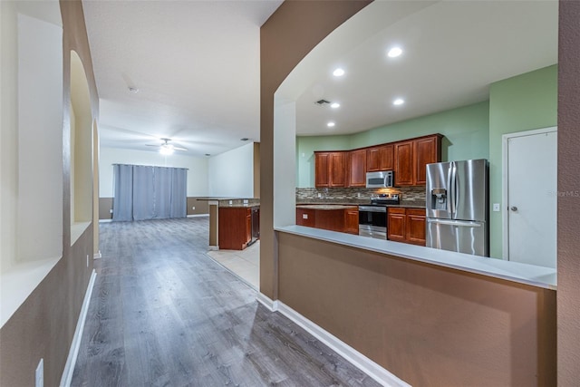 kitchen with light hardwood / wood-style flooring, appliances with stainless steel finishes, kitchen peninsula, ceiling fan, and backsplash