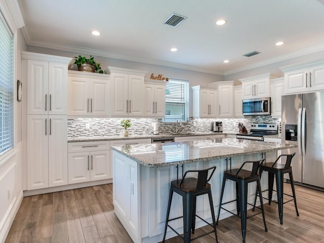 kitchen with white cabinetry, appliances with stainless steel finishes, a kitchen breakfast bar, a kitchen island, and light stone countertops