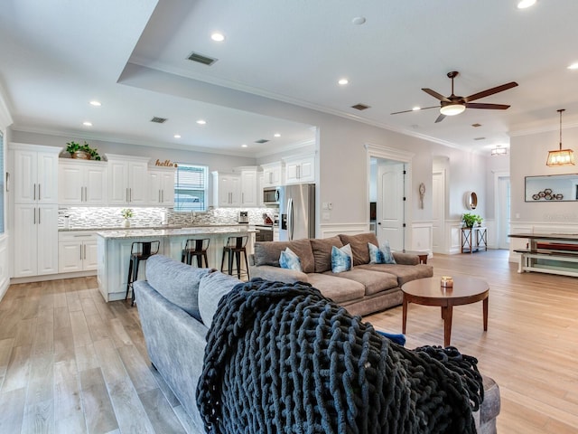 living room featuring ornamental molding, sink, ceiling fan, and light wood-type flooring